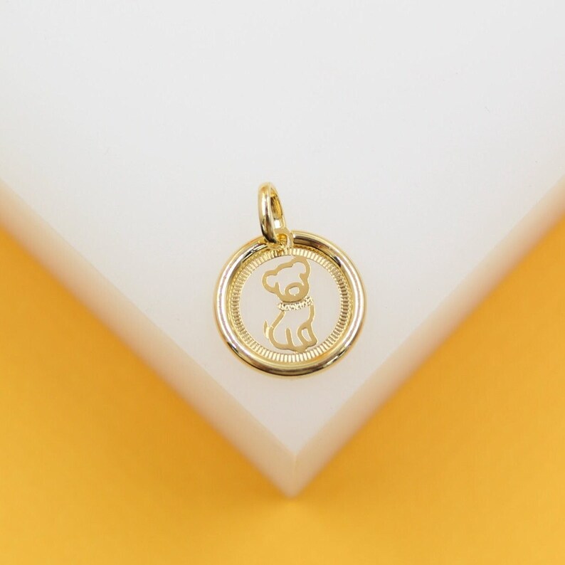 A gold pendant features an engraved silhouette of a cute dog wearing a collar inside a circular frame.