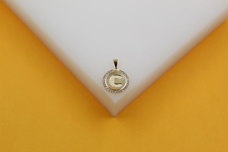 A gold initial letter C pendant rests on a geometric white and yellow display block.