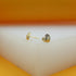 Two gold heart-shaped stud earrings sit on a white platform against an orange backdrop.