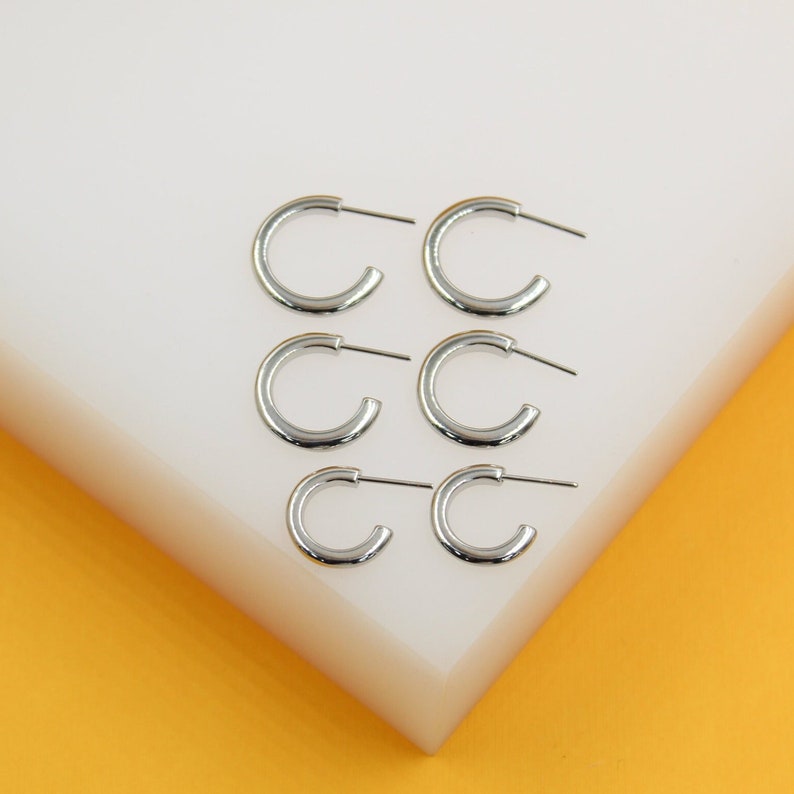 Six silver hoop earrings are arranged in two columns on a white and yellow display stand.