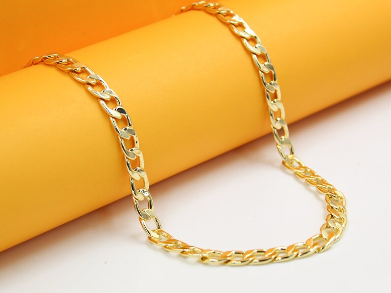 A shiny gold curb chain necklace rests gracefully against a vibrant orange and white background.