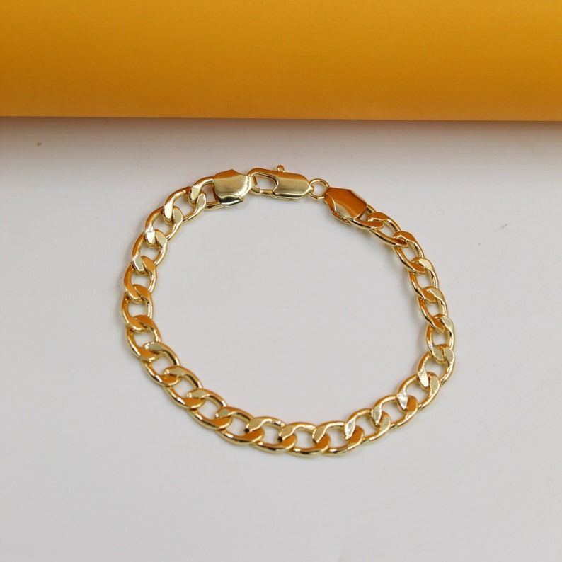 A shiny gold curb chain bracelet lies flat on a clean white surface with a yellow background.