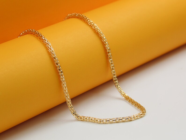 A delicate gold chain necklace rests gracefully against a vibrant orange and white display background.