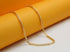 A delicate gold chain necklace rests gracefully against a vibrant orange and white display background.