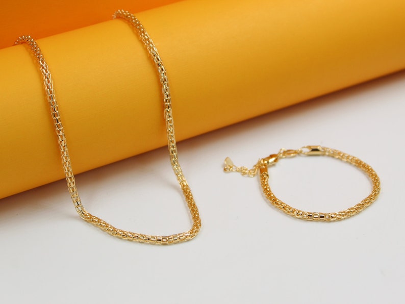 A matching gold mesh necklace and bracelet rest on a white and orange display.