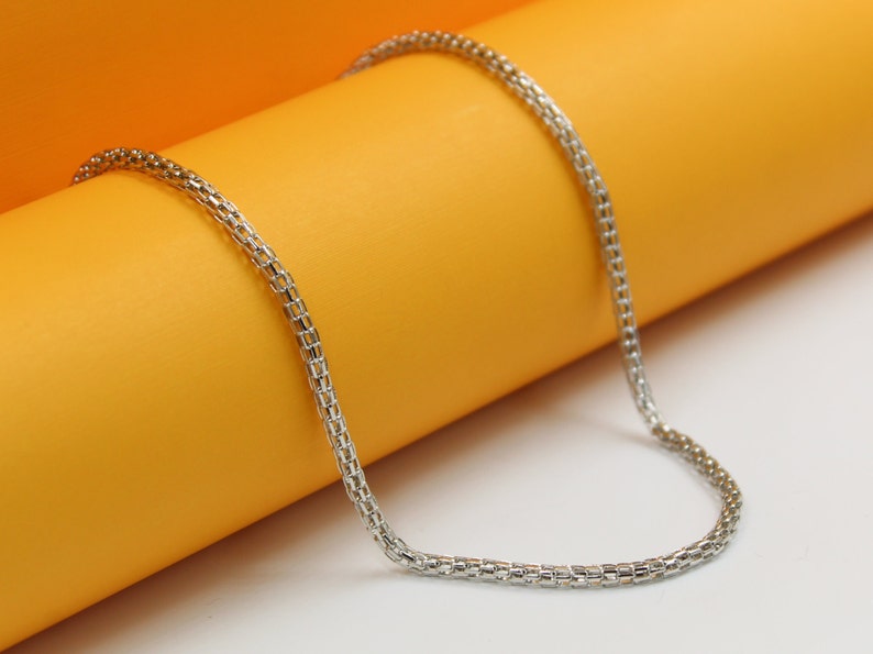 A delicate silver chain necklace rests gracefully across a vibrant orange and white display surface.