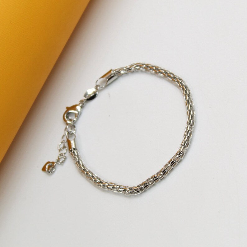 A delicate silver mesh bracelet rests on a white surface against an orange background.