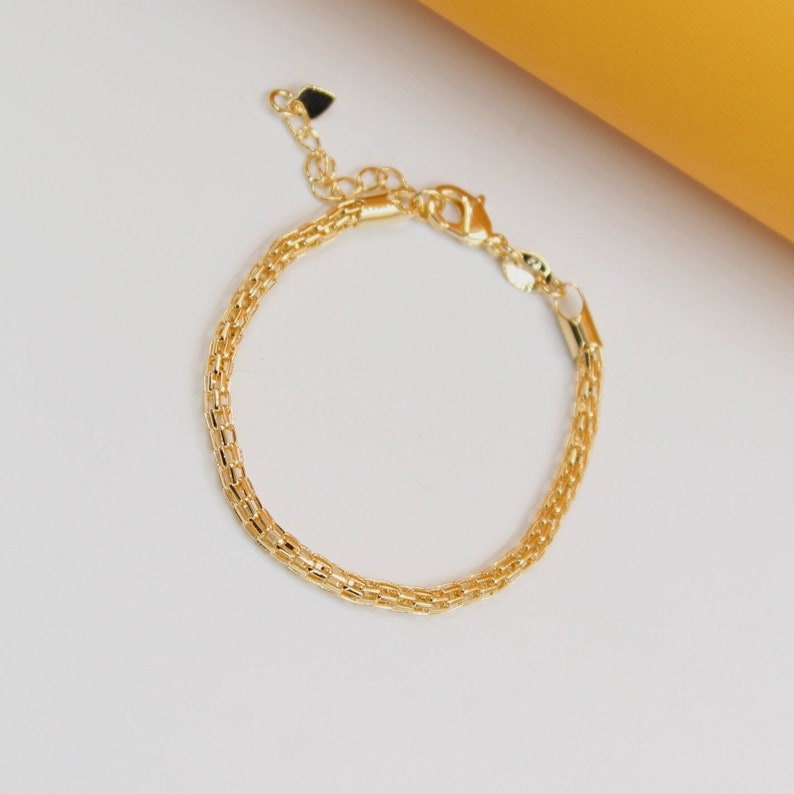 A delicate gold-plated double-strand link bracelet rests against a clean white surface.