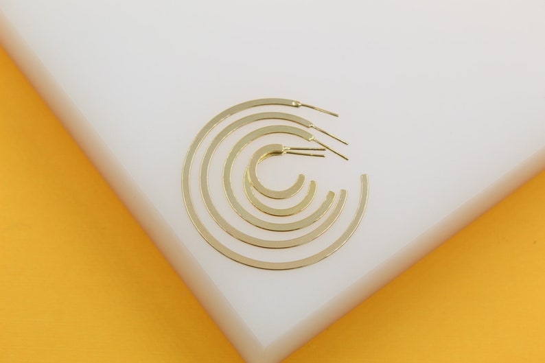 A set of graduated gold hoop earrings rests neatly on a white display surface against a vibrant yellow background.