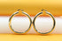 A pair of thick, polished gold hoop earrings rests against a bright yellow and white background.