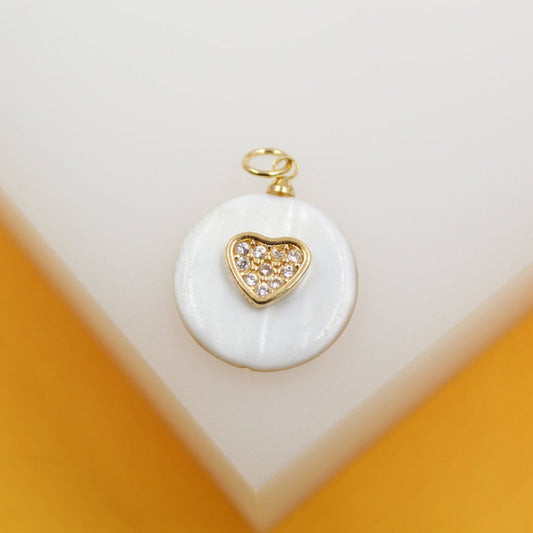 A gold and mother-of-pearl pendant features a sparkling diamond-encrusted heart resting on a white shell circle.