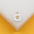 A gold-rimmed white pendant featuring a pave diamond heart rests on a white display surface.