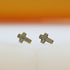 A pair of gold cross stud earrings sparkle with embedded cubic zirconia stones against a soft white and orange background.