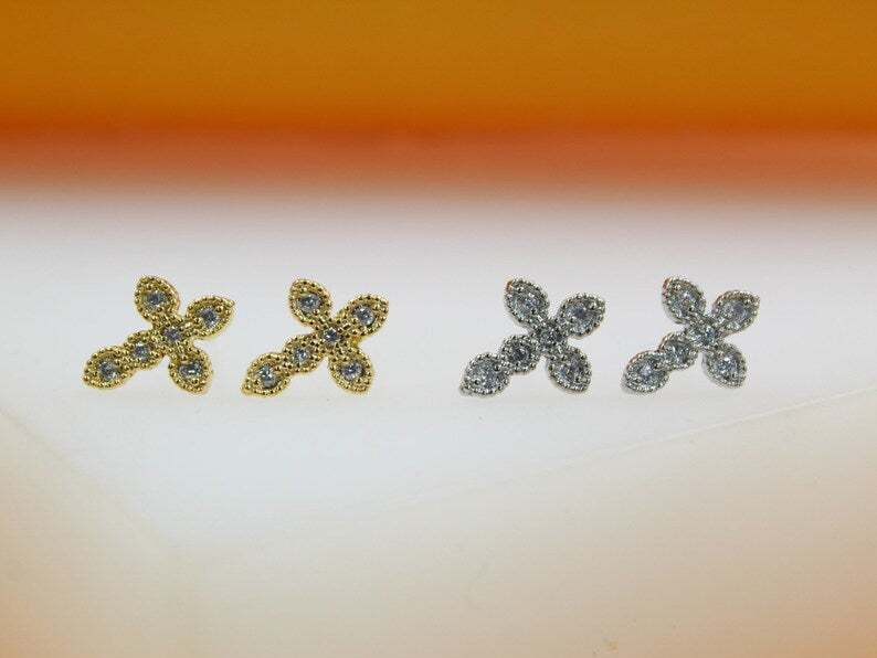 Two pairs of delicate cross-shaped stud earrings, one in gold and one in silver, sparkle against a neutral background.