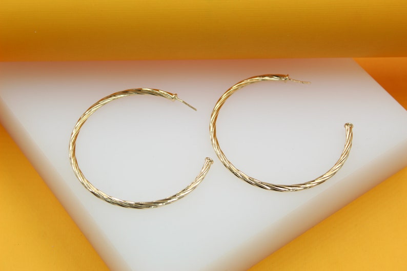A pair of elegant twisted gold hoop earrings rests on a white and orange display surface.