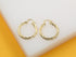 A pair of shiny twisted gold hoop earrings rests on a white and yellow display surface.