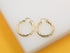 A pair of polished gold twist hoop earrings rests on a white display surface.
