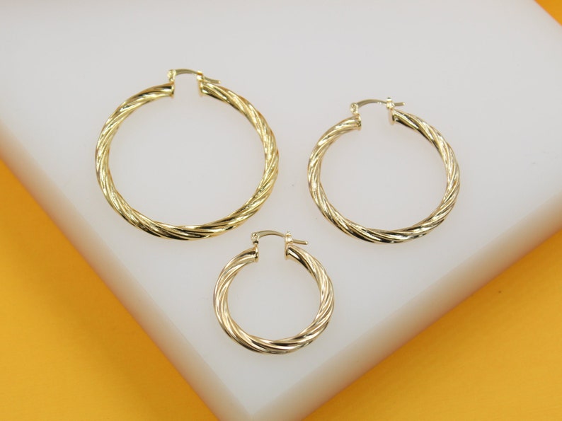 Three polished gold twisted hoop earrings in graduated sizes display their intricate rope design on a white surface.