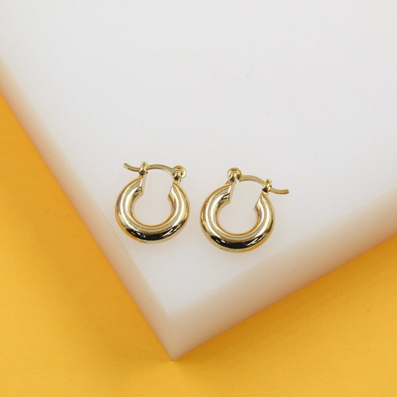 A pair of polished gold hoop earrings rests neatly on a white display block.
