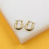 A pair of polished gold hoop earrings rests neatly on a white display block.