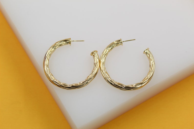A pair of textured gold hoop earrings rests on a white display surface.