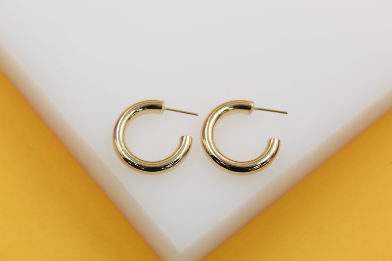 A pair of polished gold hoop earrings rests side-by-side on a clean white display surface.