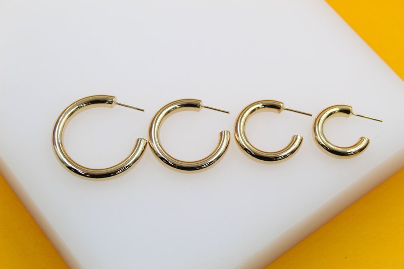 Four polished gold hoop earrings in graduated sizes lie arranged in a row on a white display surface.