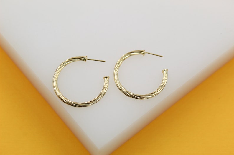 A pair of twisted gold hoop earrings rests neatly on a white display surface.
