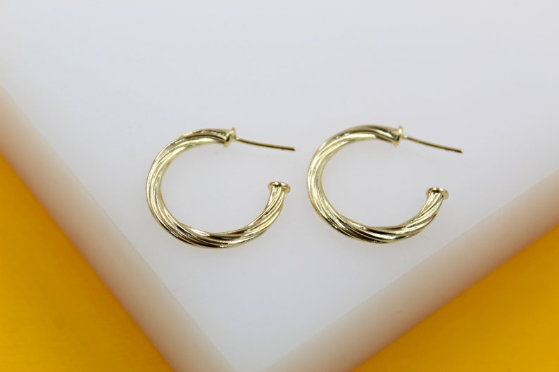 A pair of twisted gold hoop earrings rests on a white display surface.