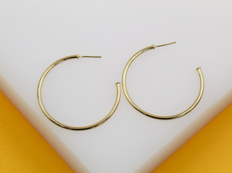A pair of elegant gold hoop earrings rests on a white display surface.