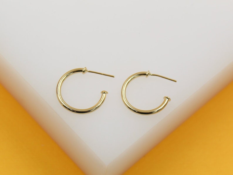 A pair of sleek gold hoop earrings rests side-by-side on a clean white display surface.