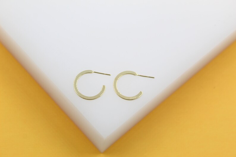 A pair of minimalist gold hoop earrings rests neatly on a clean white display surface.