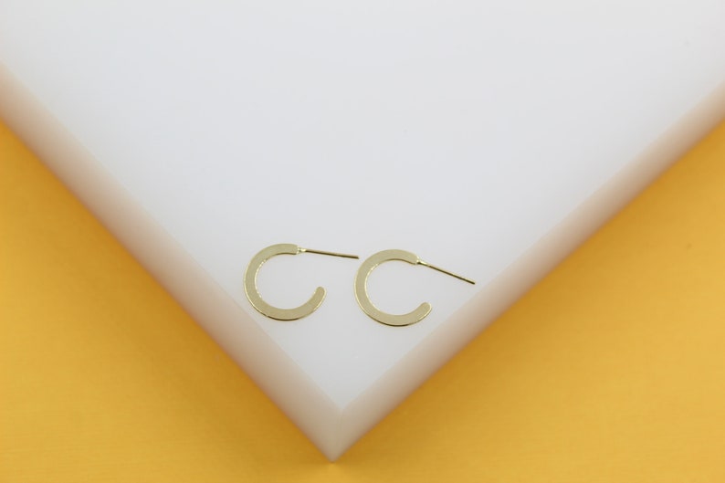 A pair of minimalist gold hoop earrings rests neatly on a clean white display block.