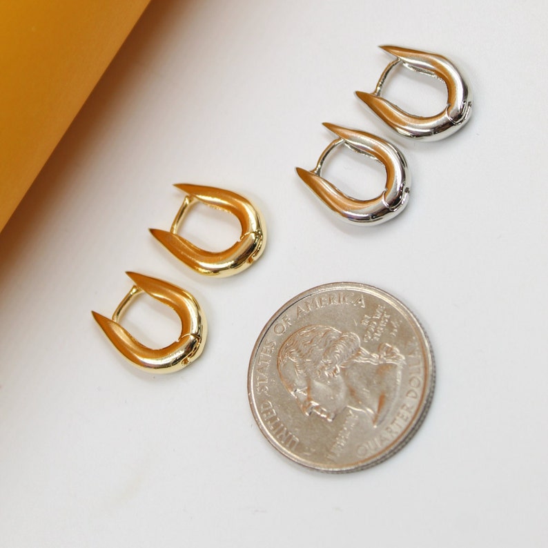 Two pairs of glossy gold and silver U-shaped huggie hoop earrings sit next to a US quarter coin on a white surface.