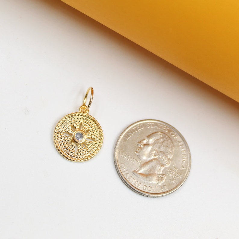 A gold compass pendant with a central cubic zirconia stone rests next to a US quarter for scale.