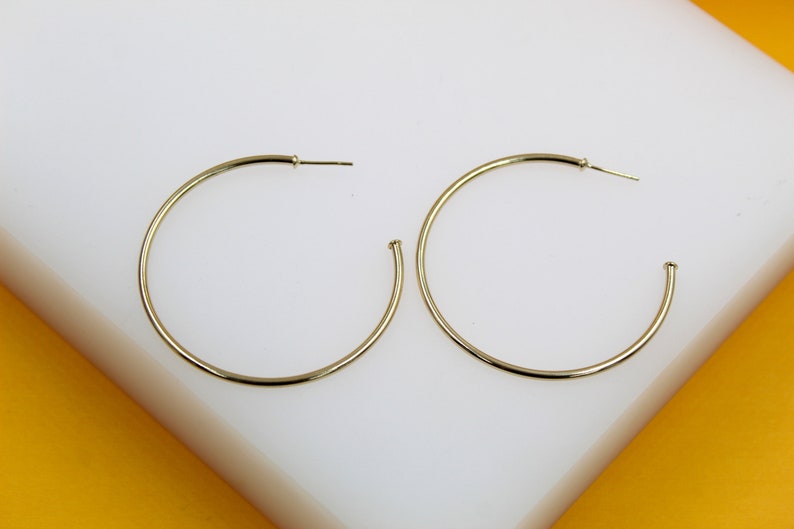 A pair of sleek gold hoop earrings rests gracefully on a white display surface.