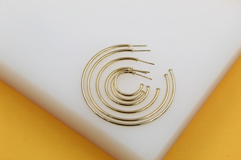 A set of nested gold hoop earrings of varying sizes rests on a white display surface.