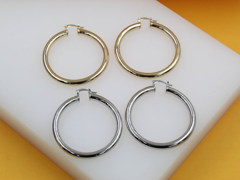 Four polished hoop earrings in gold and silver display classic everyday style on a white display block.
