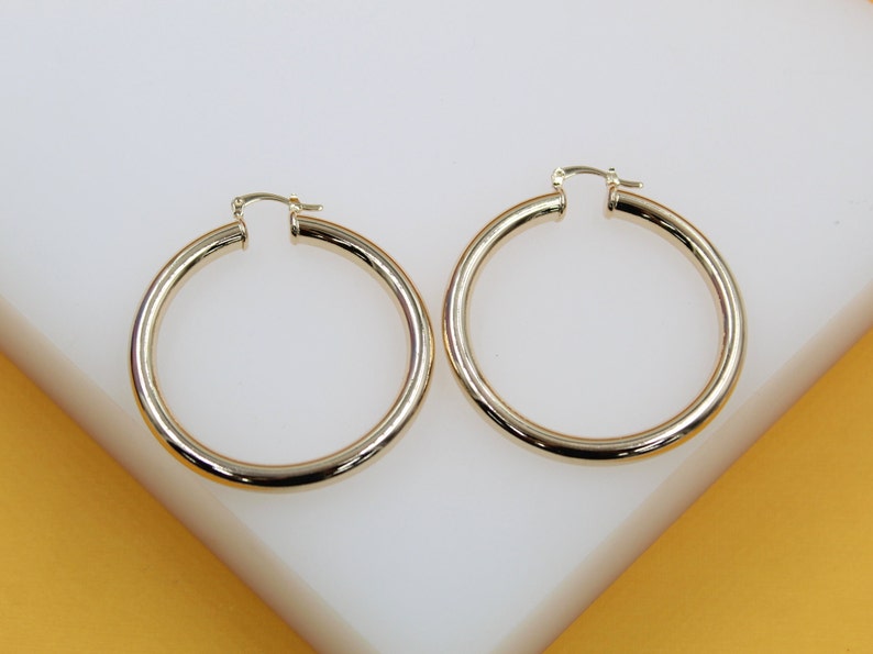 A pair of polished gold hoop earrings rests on a white display surface.