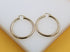 A pair of polished gold hoop earrings rests on a white display surface.