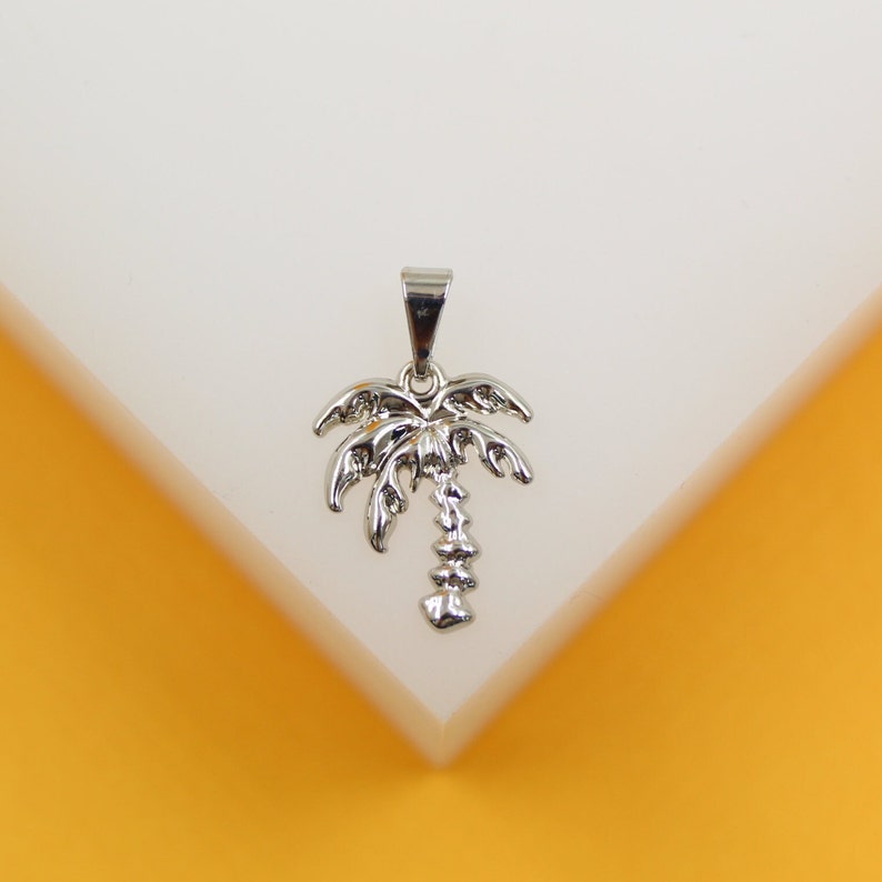 A silver palm tree pendant rests on a clean white and yellow display surface.