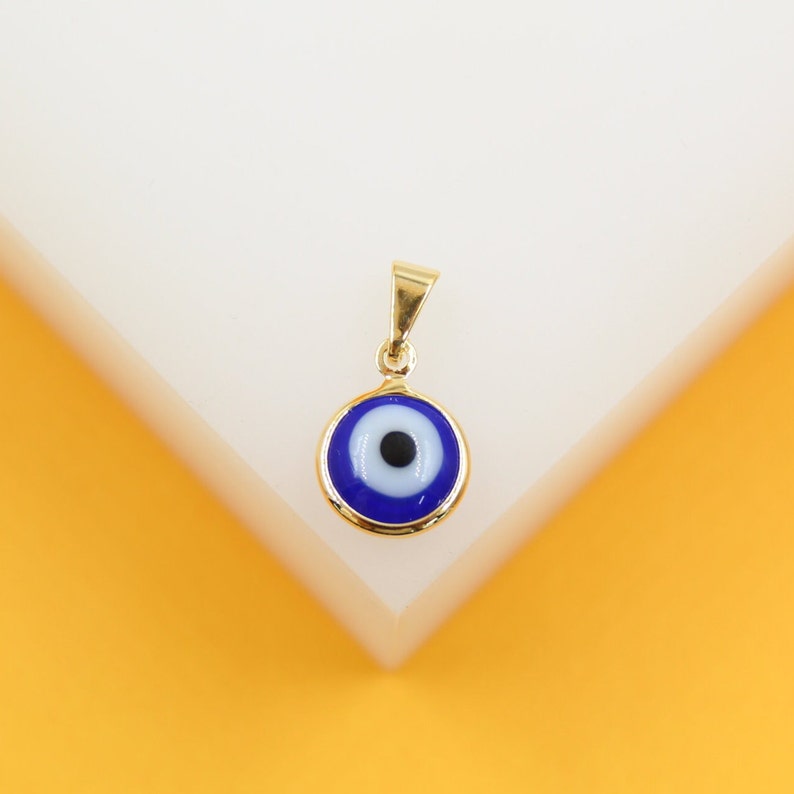A gold evil eye pendant rests on a clean white and yellow display stand.