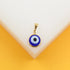A gold evil eye pendant rests on a clean white and yellow display stand.