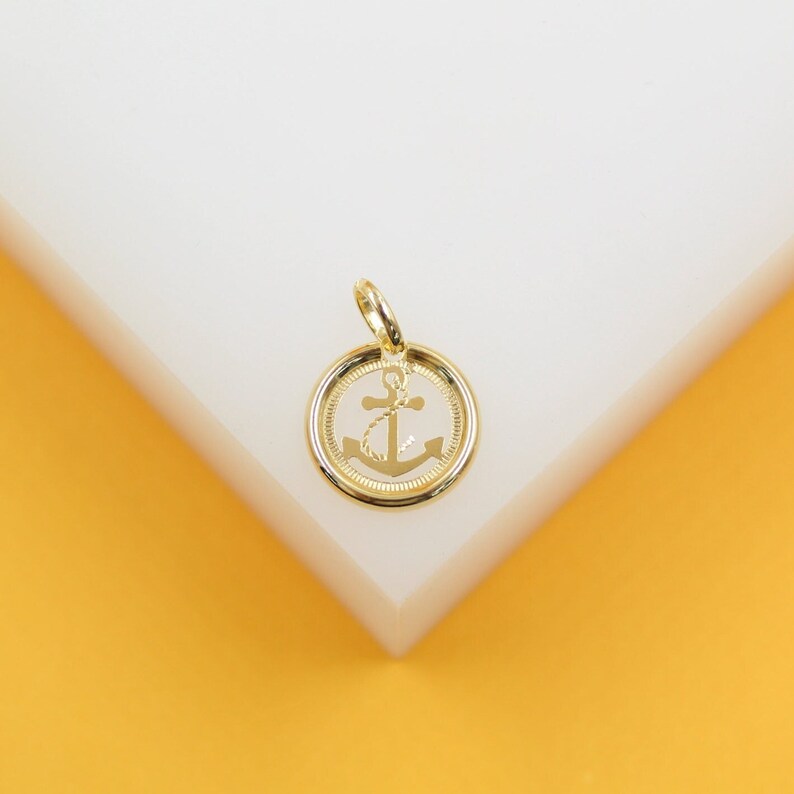 A gold anchor pendant rests on a white and yellow display stand.