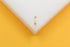A delicate gold lightning bolt charm rests on a white display surface against a vibrant yellow background.