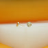 A pair of round, textured gold stud earrings rests on a white surface against an orange background.