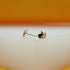 A pair of glossy gold heart-shaped stud earrings rests on a white surface against an orange backdrop.