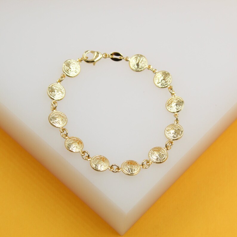 A gold coin charm bracelet rests on a white and yellow display stand.