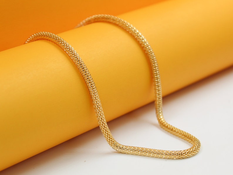 A textured gold chain necklace rests gracefully against a vibrant yellow and white background.