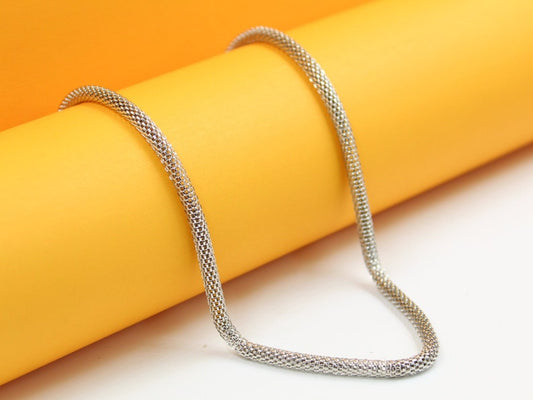 A gleaming silver mesh necklace drapes elegantly across a vibrant yellow cylinder background.
